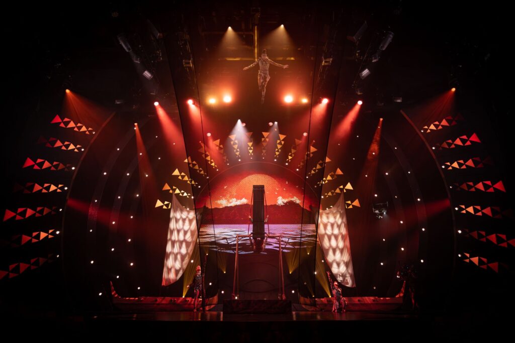 Wide stage view of Cirque du Soleil’s Auana production with vibrant lighting and a large circular backdrop.