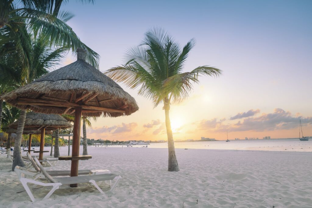 Beach sunset with palm trees and lounge chairs on soft white sand, tranquil tropical setting, relaxing oceanfront view.