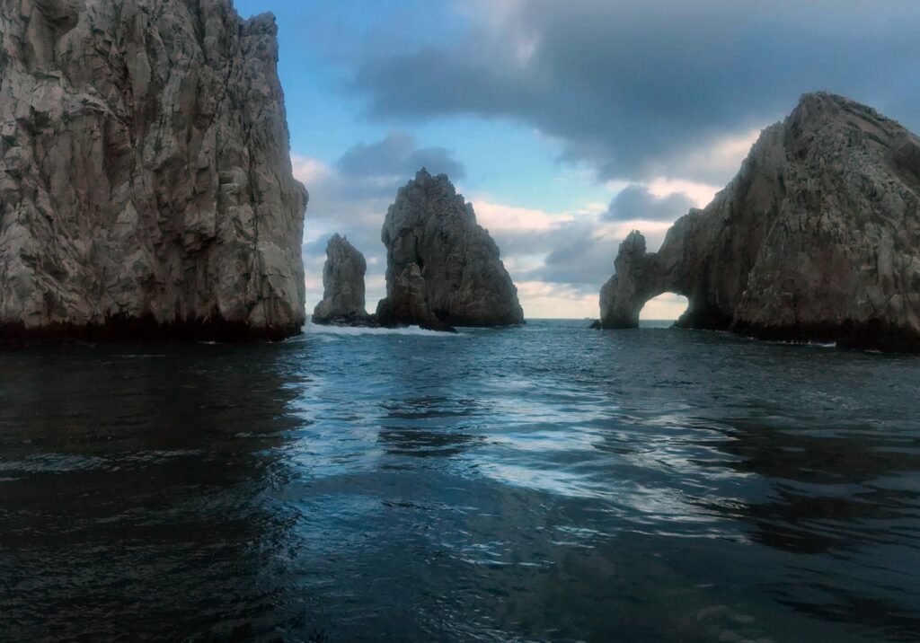 Dramatic ocean view of El Arco de Cabo San Lucas with rugged rock formations rising from deep blue waters under a bright sky.