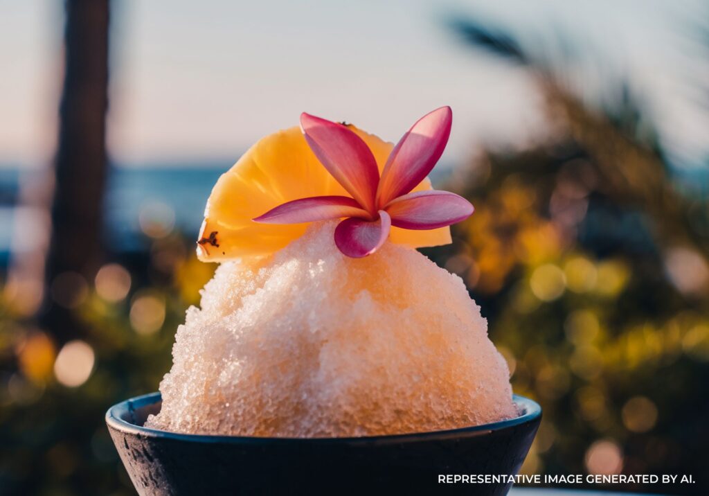 Close up shot of Hawaiian shave ice topped with pineapple and a flower at the beach.