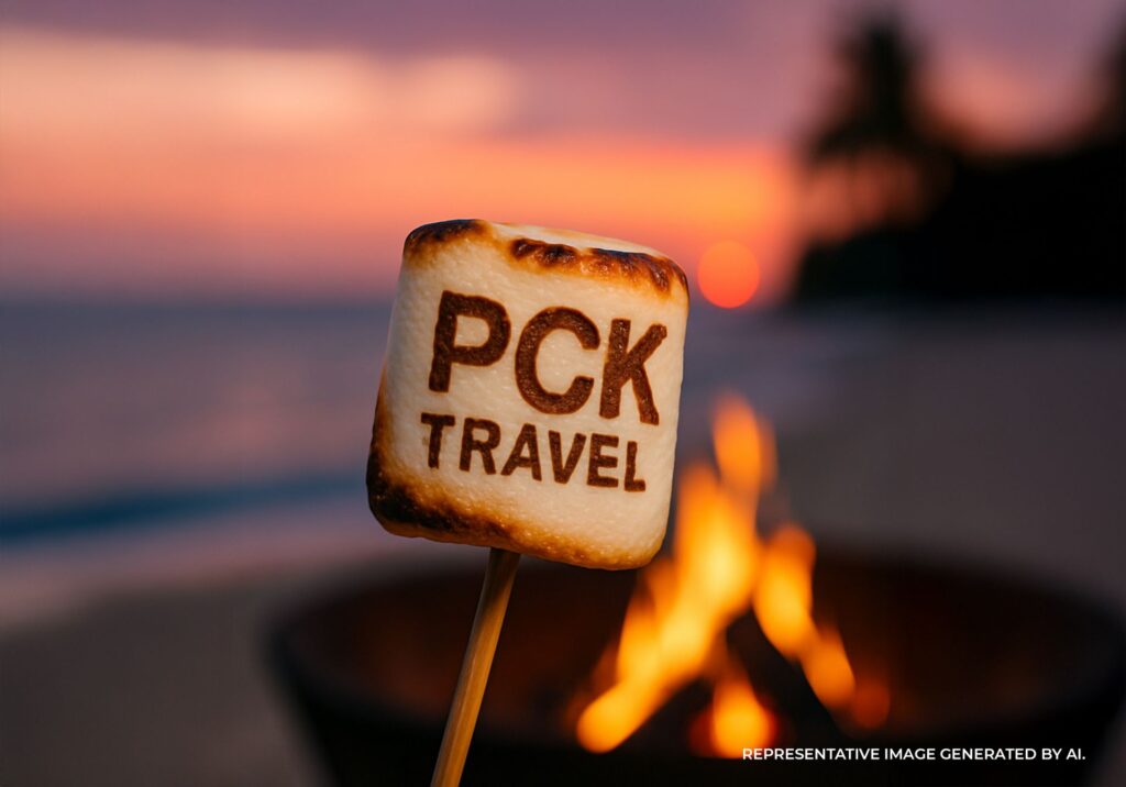 Toasted marshmallow with the PCK Travel logo held over a beach bonfire at sunset with the ocean and palm trees in the background.