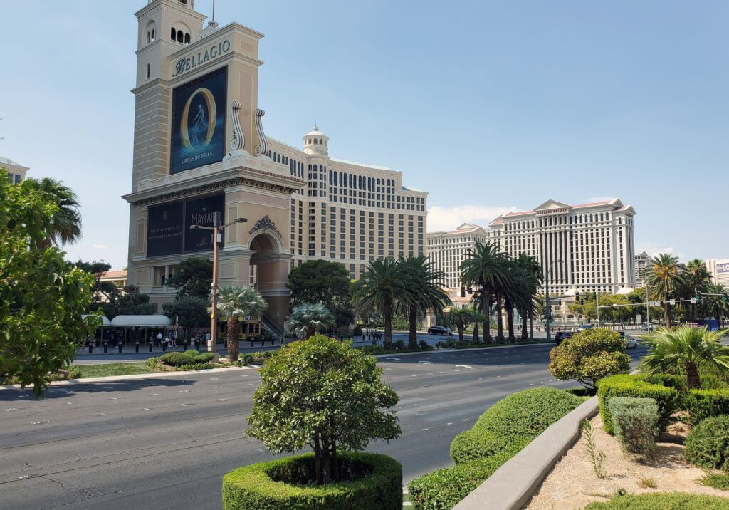Street view of the Bellagio and Caesars Palace along Las Vegas Boulevard surrounded by palm trees and sunshine.
