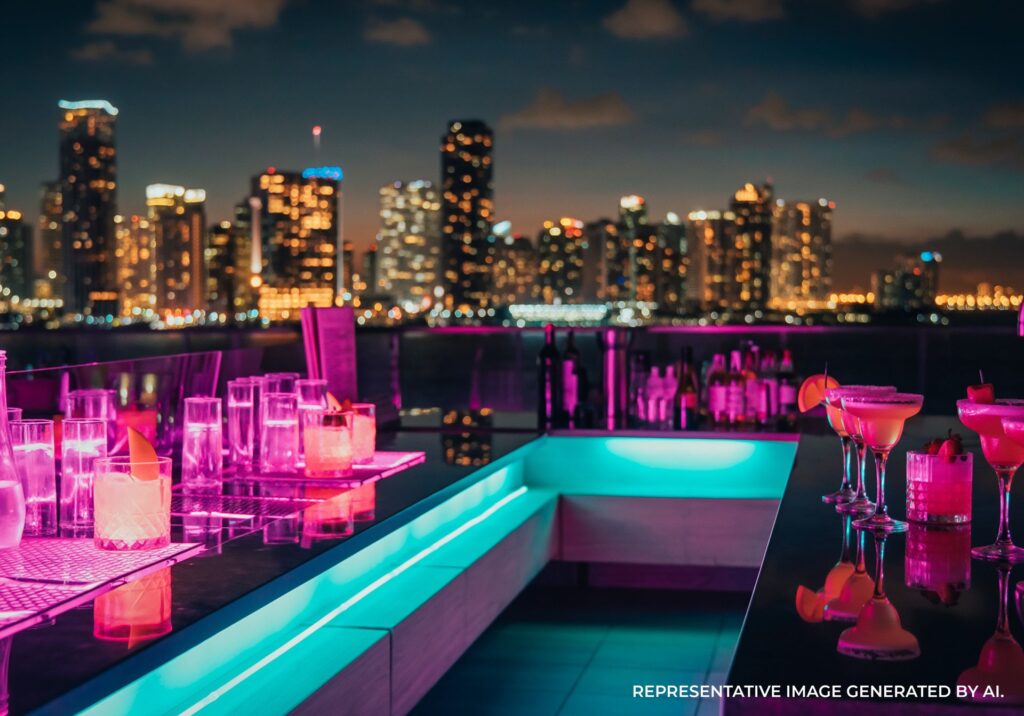 Rooftop pool and lounge seating lit by neon lights with skyline backdrop.