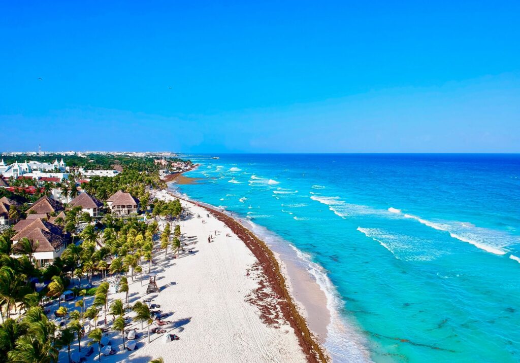 Aerial view of Playa del Carmen coastline showing resorts, palm trees, and turquoise Caribbean waves.