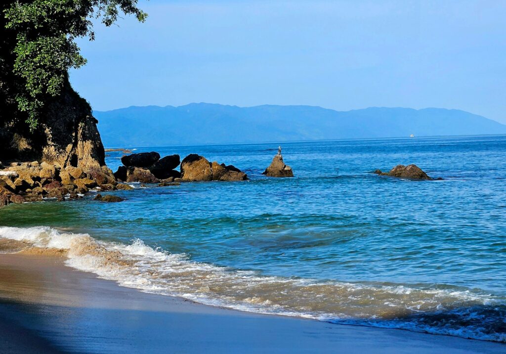 Blue waves breaking against shoreline rocks with distant mountains in Puerto Vallarta