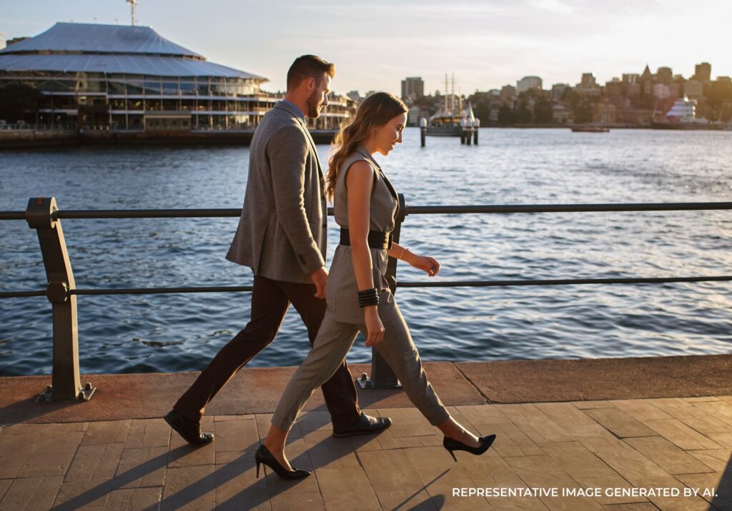 Couple walking along a Sydney waterfront boardwalk with city views.