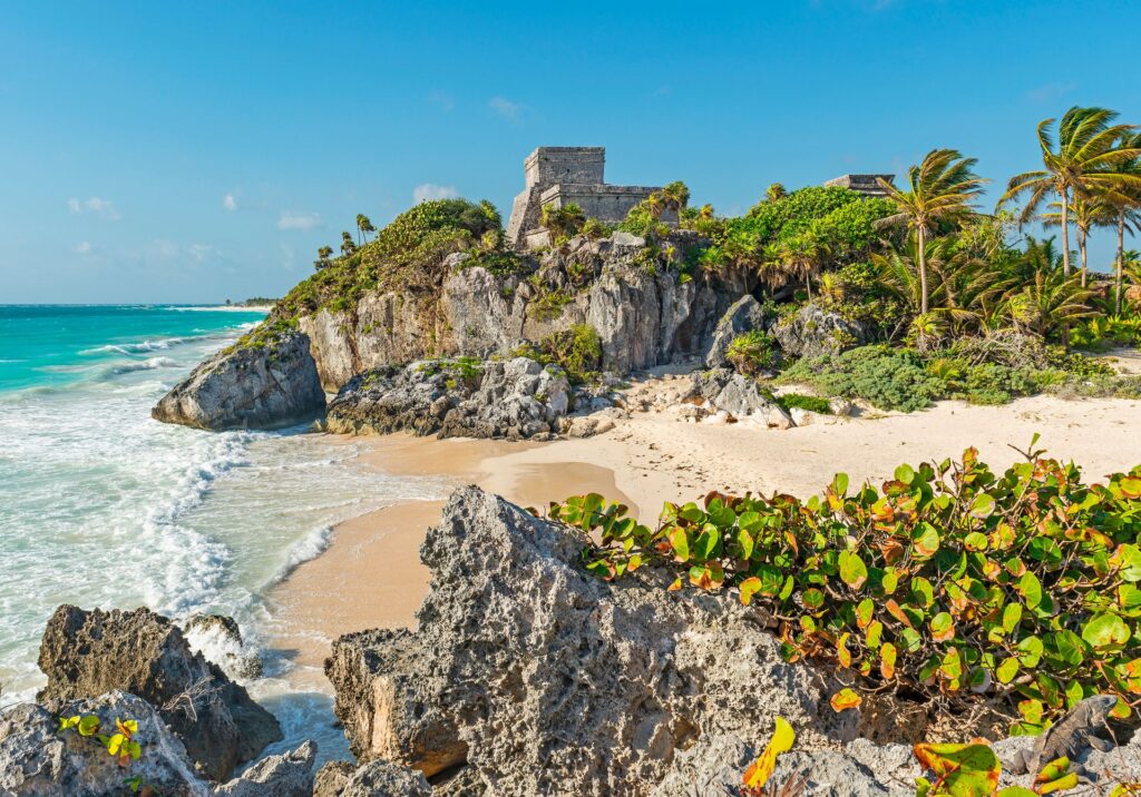 Ancient Mayan ruins of Tulum perched above turquoise Caribbean waters with lush tropical plants.