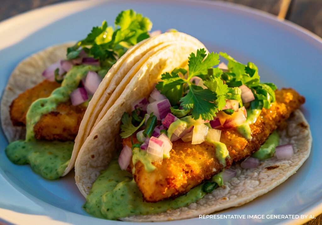 Colorful fish tacos with toppings on a wooden table near the beach.