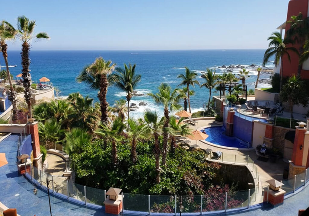 Resort pool with sun loungers by the water and palm trees overlooking the ocean in Cabo San Lucas Mexico