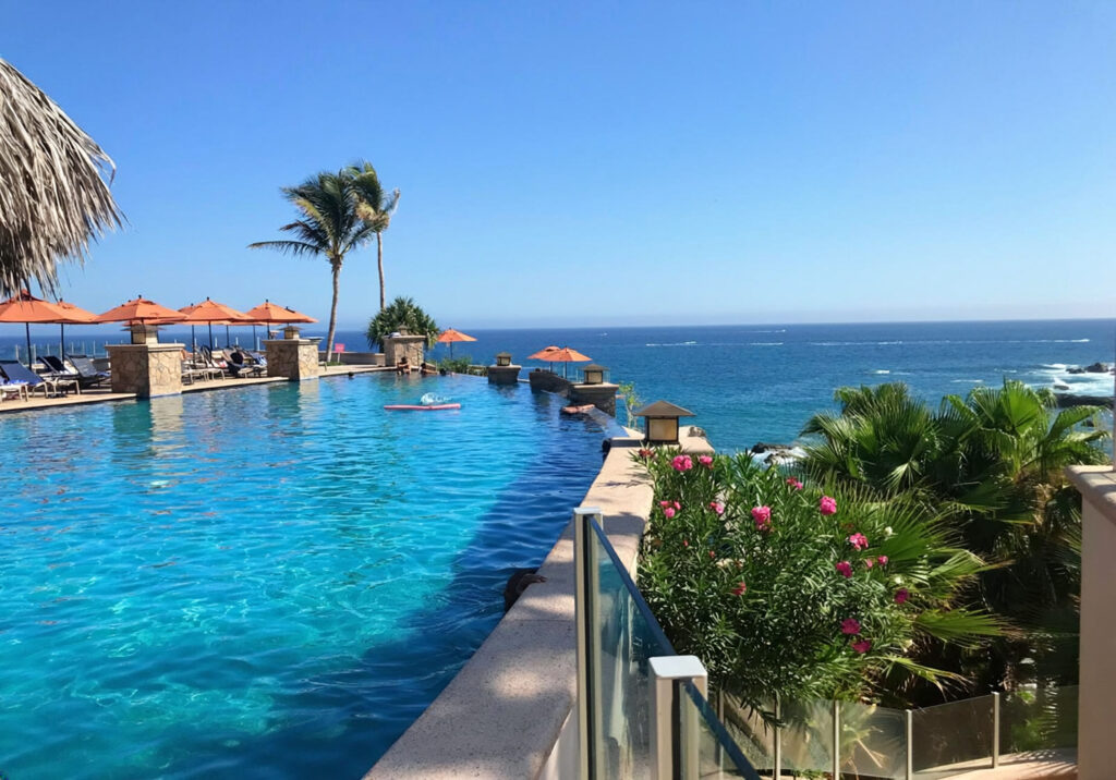 Luxury infinity pool overlooking the ocean with palm trees and lounge chairs at a beachfront resort in Cabo San Lucas Mexico