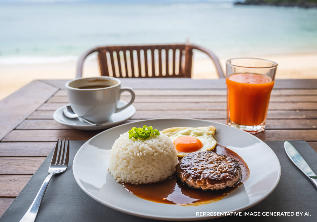 A loco moco breakfast plate served with white rice, coffee, and tropical juice on a wooden table overlooking the ocean Kaua'i.