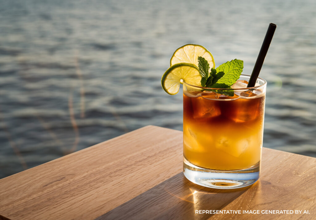 A Mai Tai cocktail garnished with lime and mint on a wooden table overlooking the ocean at sunset on the Island of Hawaiʻi.