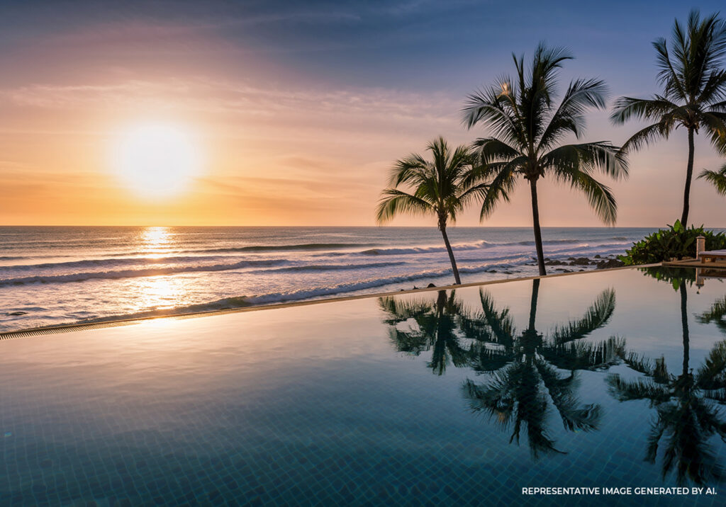 Resort infinity pool reflecting palm trees at sunset beside the ocean.