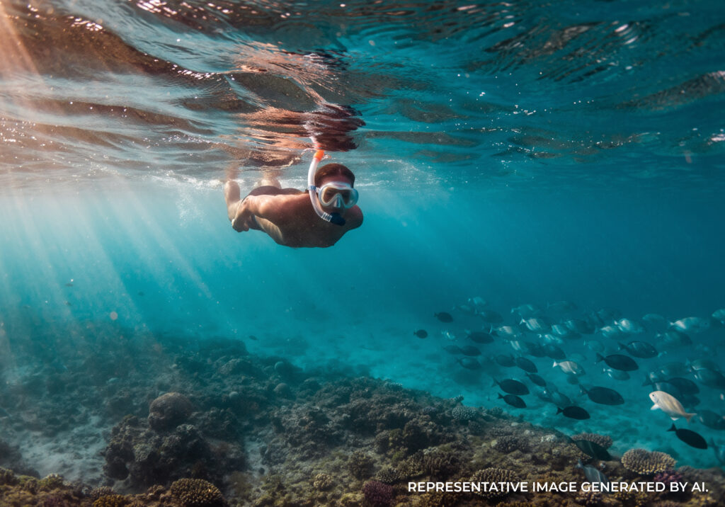 Female snorkeler underwater with sun rays shining through clear water above coral reef in Kauaʻi.