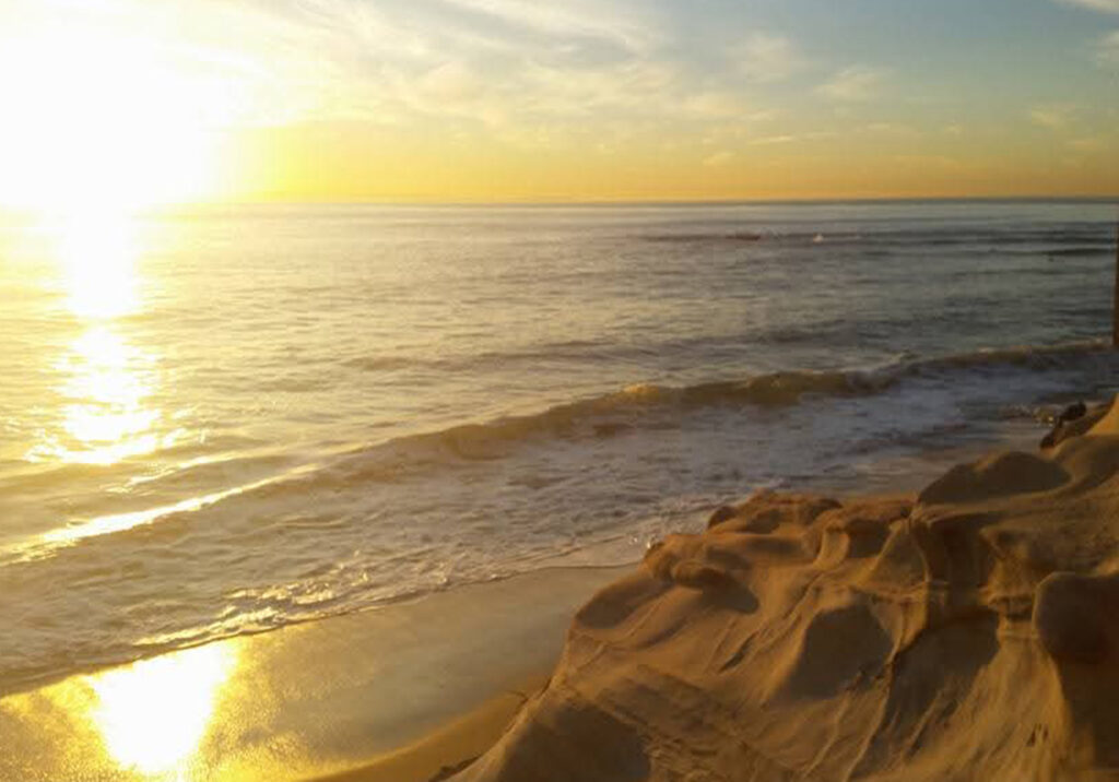 Sunset reflecting off wet sand at Newport Beach, California with soft waves washing onto the shoreline.