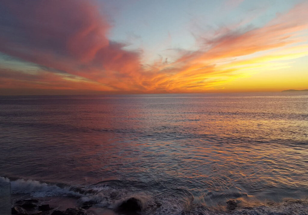 Sunset over the Pacific Ocean at Newport Beach, California with soft waves rolling toward the shore beneath colorful evening clouds.
