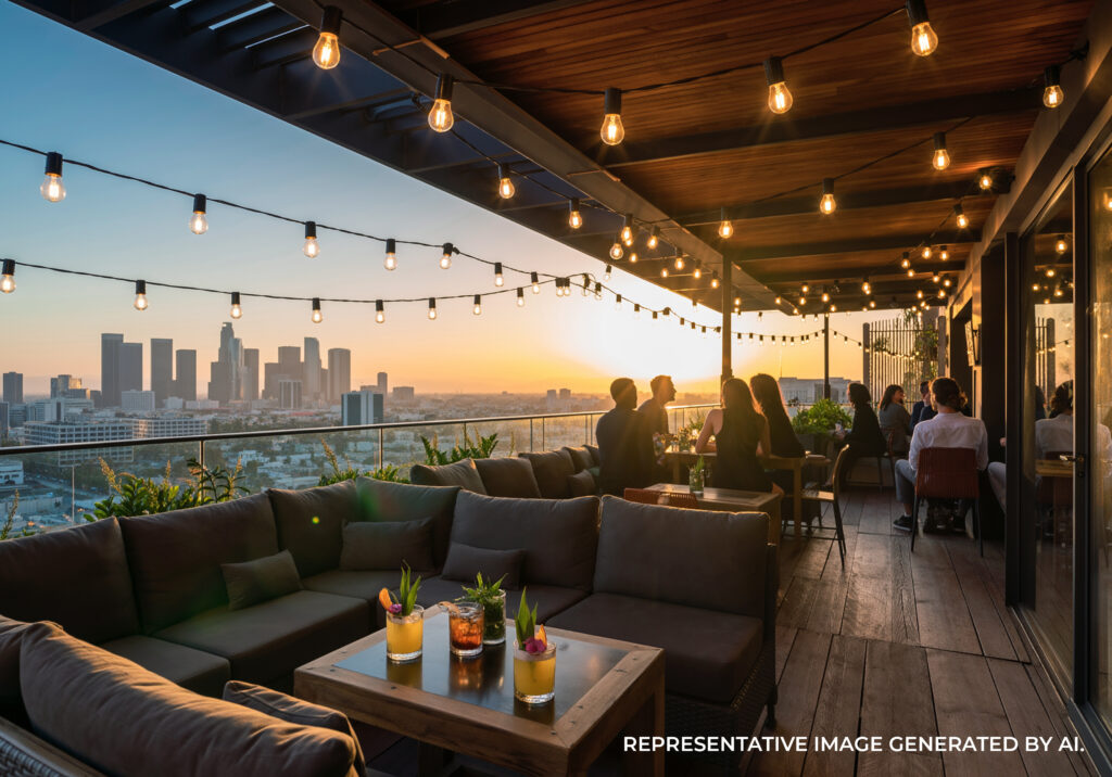 Outdoor dining tables on a patio lined with palm trees and string lights at sunset.