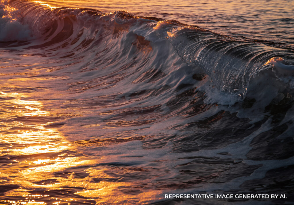 A large ocean wave curling toward the viewer with warm orange sunset light on the water.