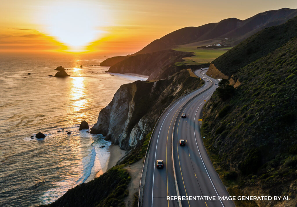 A coastal highway curving along rugged cliffs with the ocean below during golden hour.