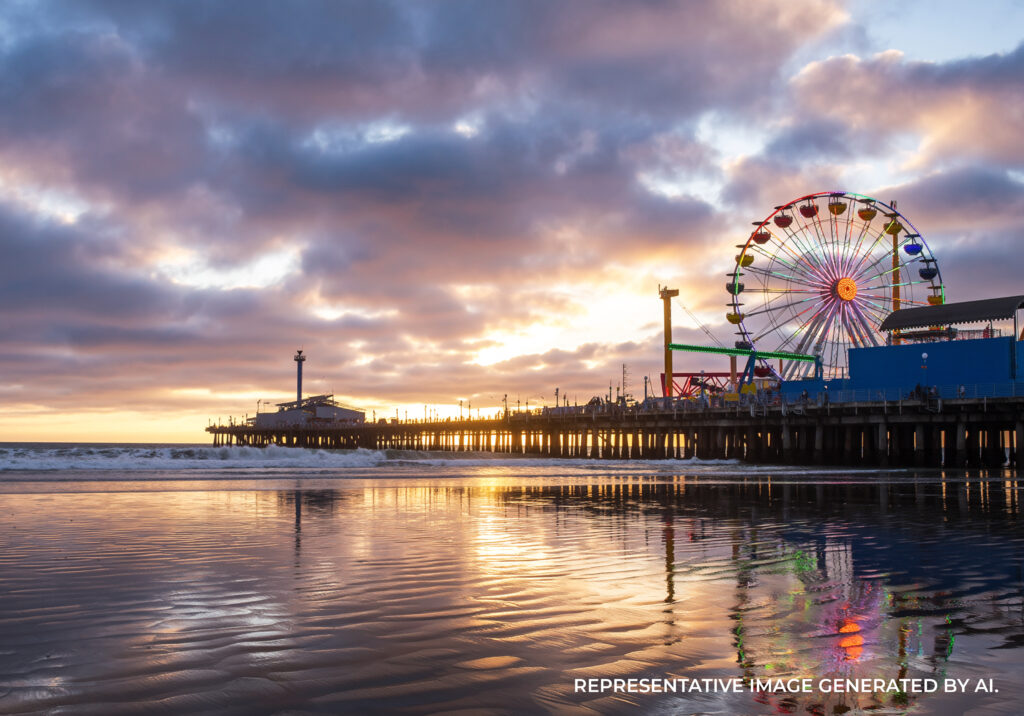 Santa Monica Pier and amusement park rides illuminated at sunset with reflections in the ocean water.