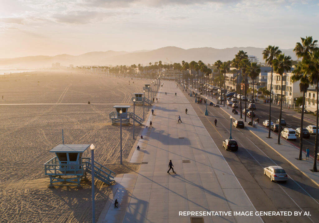 A wide view of a beachside walkway with people walking, skating, and cycling near the shoreline.