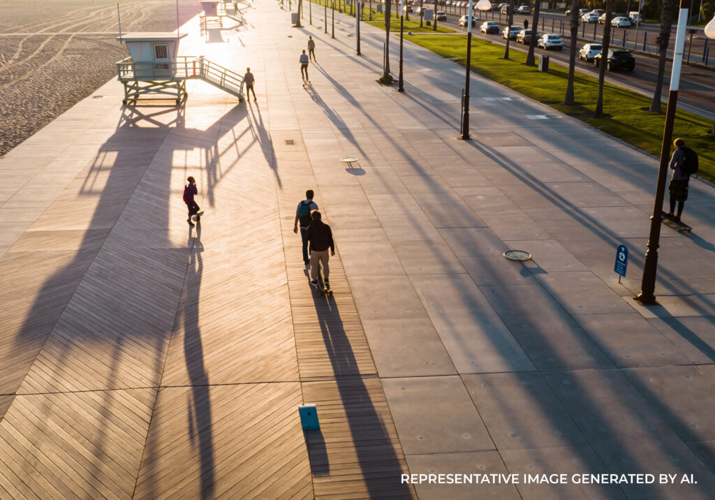 A palm lined boardwalk with a cyclist riding in warm afternoon light near the beach.