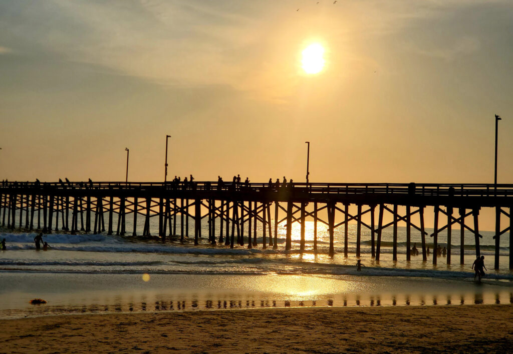 Sunset view of the Newport Beach Pier in California with warm sunlight reflecting on the sand and ocean.