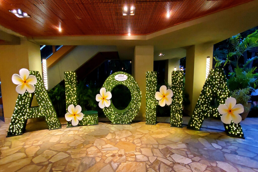 A decorative floral “ALOHA” sign inside a stylish Oʻahu mall with warm lighting and tropical greenery.