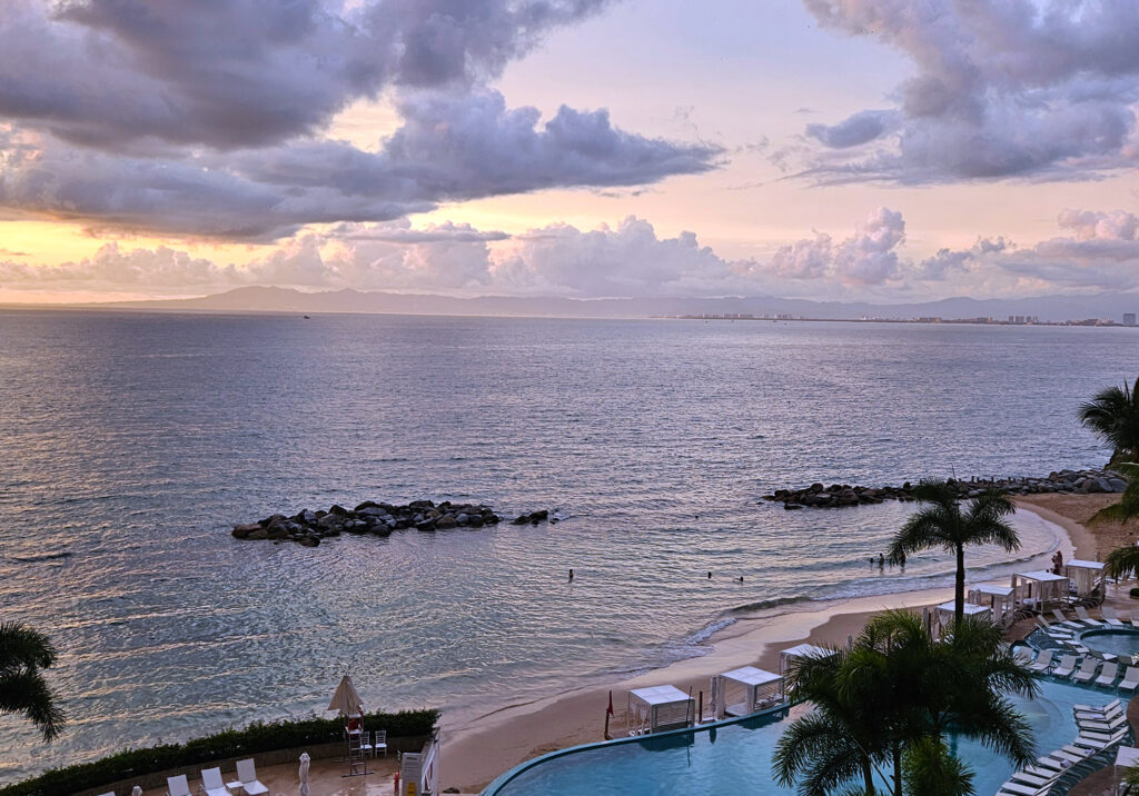 Gentle sunset reflecting over calm ocean water along the Puerto Vallarta coastline near a beachfront pool area