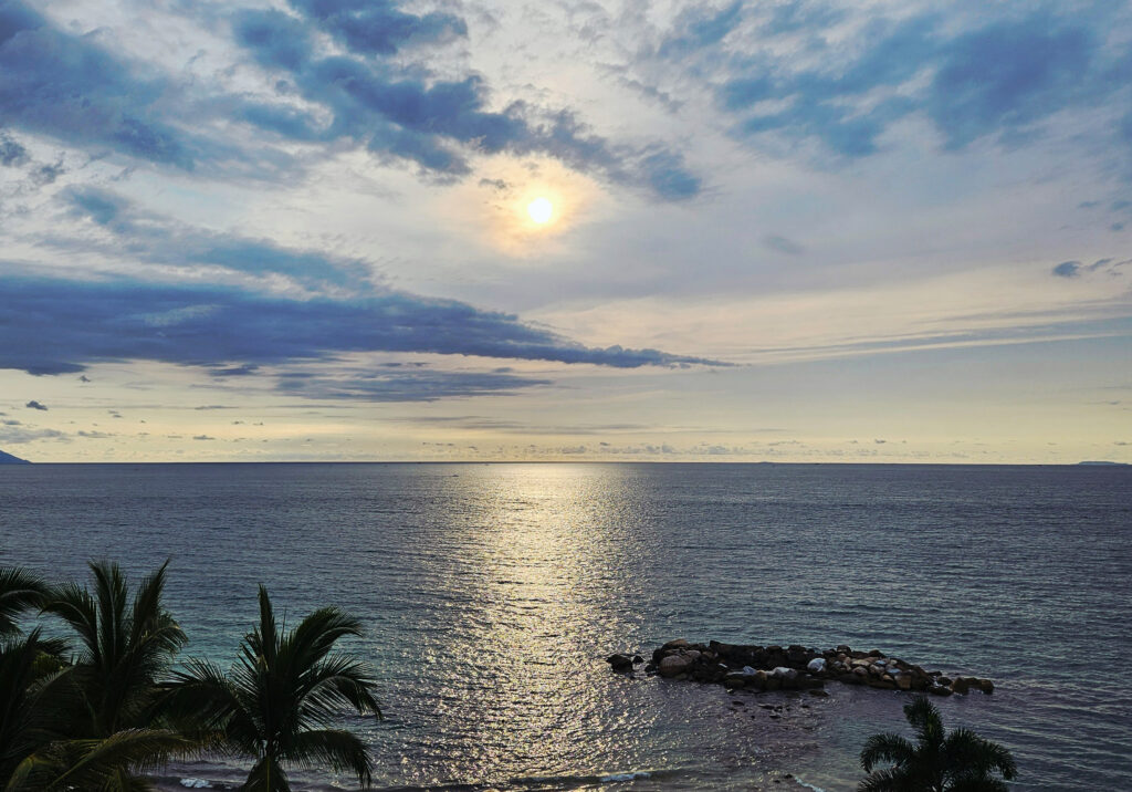 A warm sunset casts soft golden light across the calm Puerto Vallarta shoreline with gentle waves