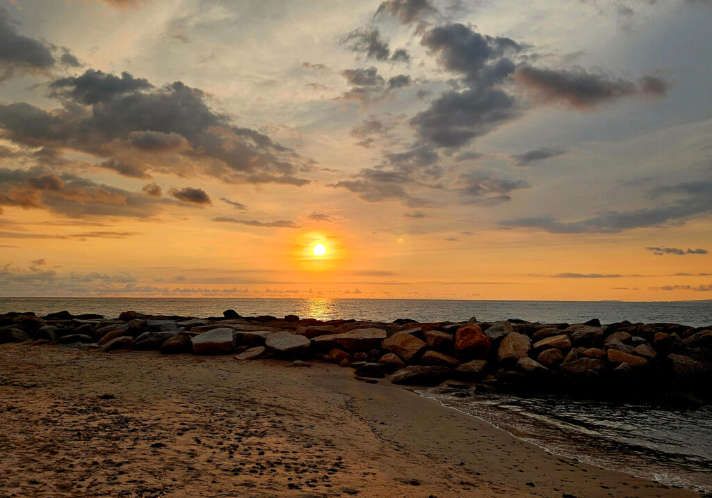 A golden sunset reflects across a rocky beach in Puerto Vallarta with warm clouds above