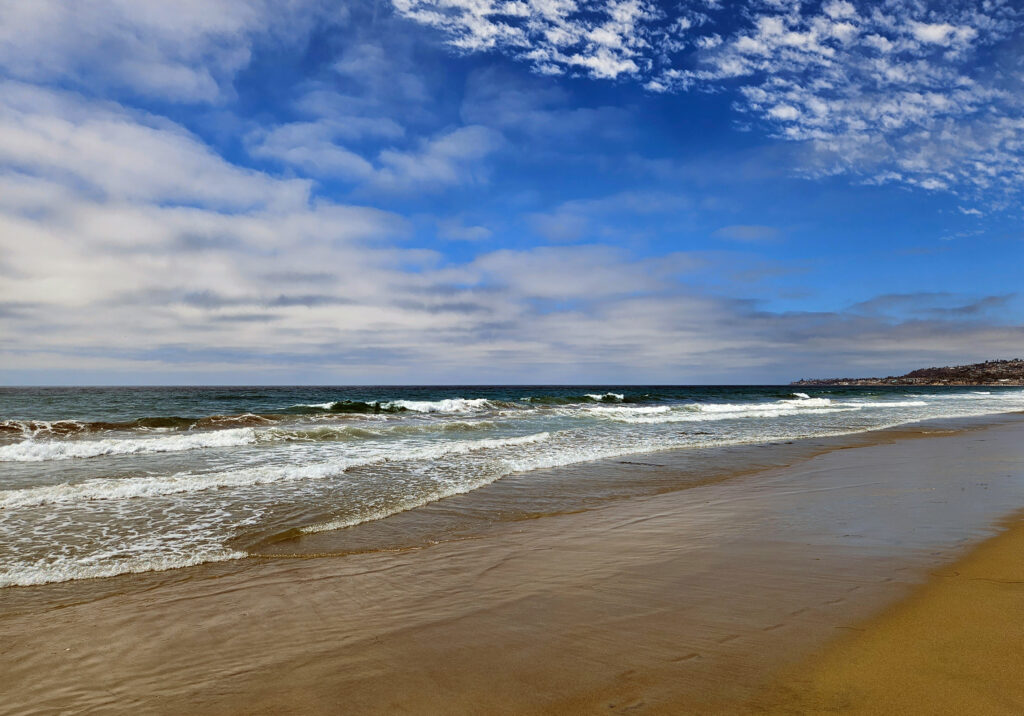 Wide sandy beach with waves and a bright blue sky along the oceanfront.