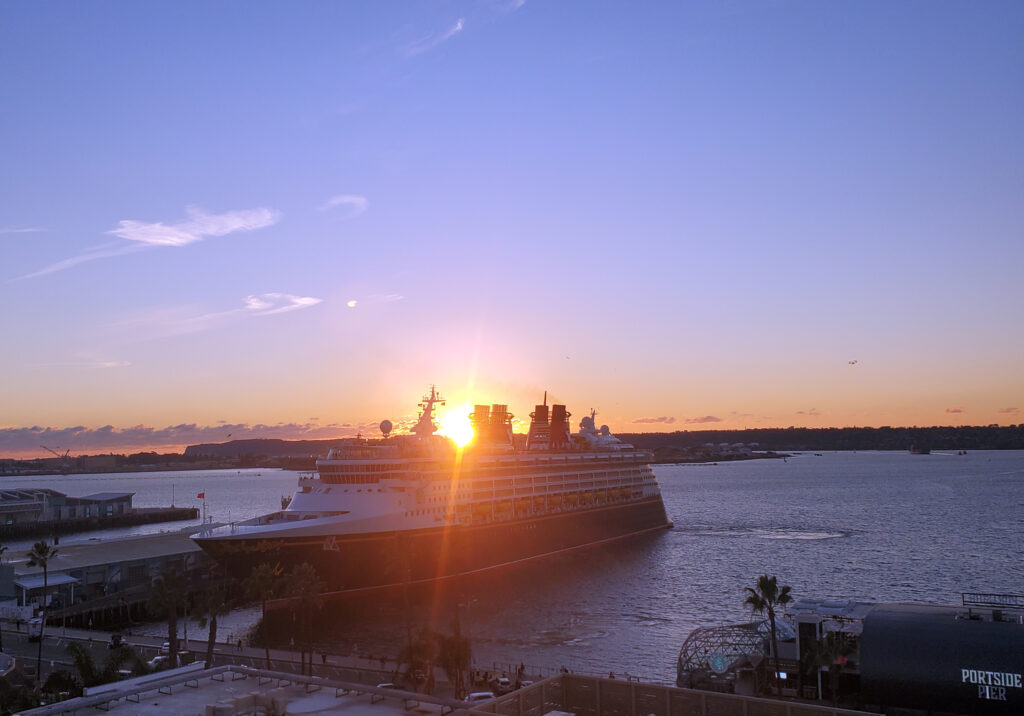 cruise ship docked in San Diego Bay under a colorful dusk sky with reflections on the water