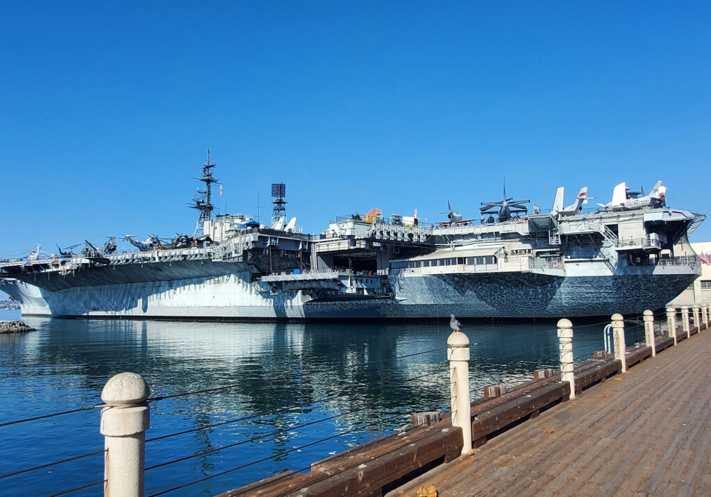 USS Midway aircraft carrier floating beside a pier in San Diego Harbor on a sunny day.