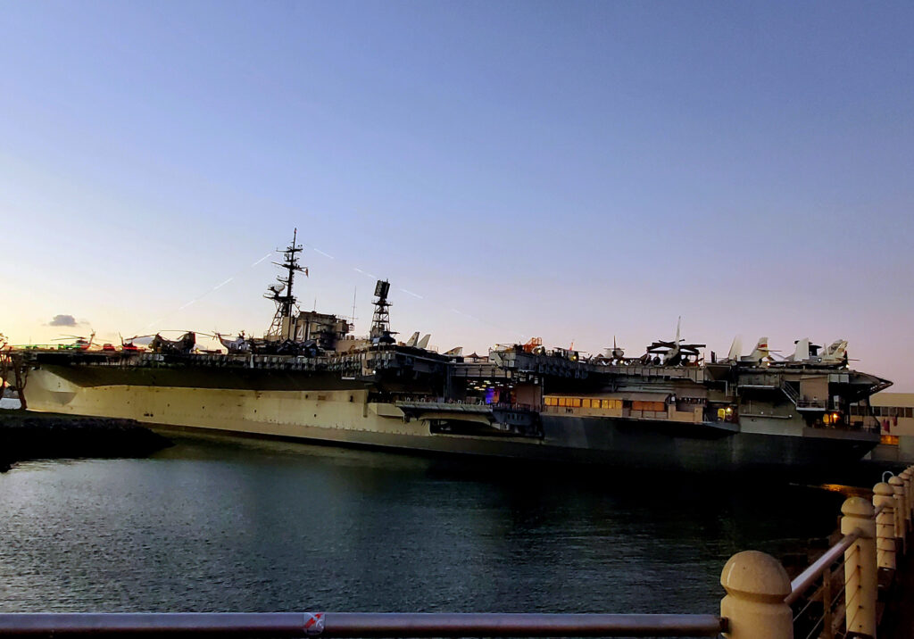 USS Midway Museum with downtown San Diego skyline and harbor waters at sunset.