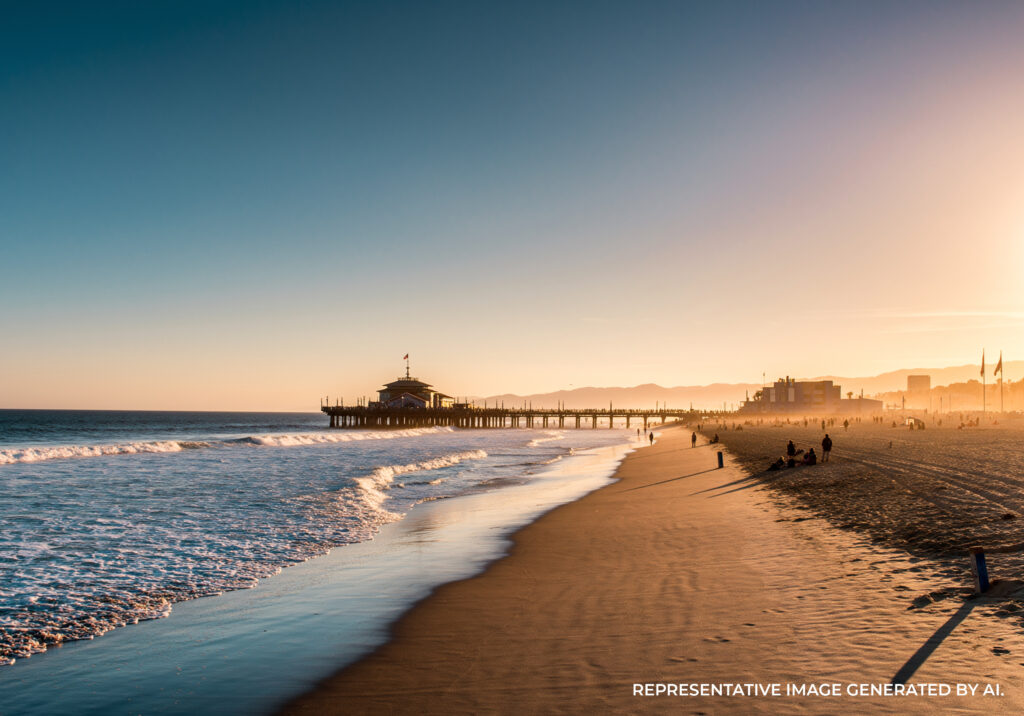 A sandy beach with gentle waves and a distant pier under golden evening light.