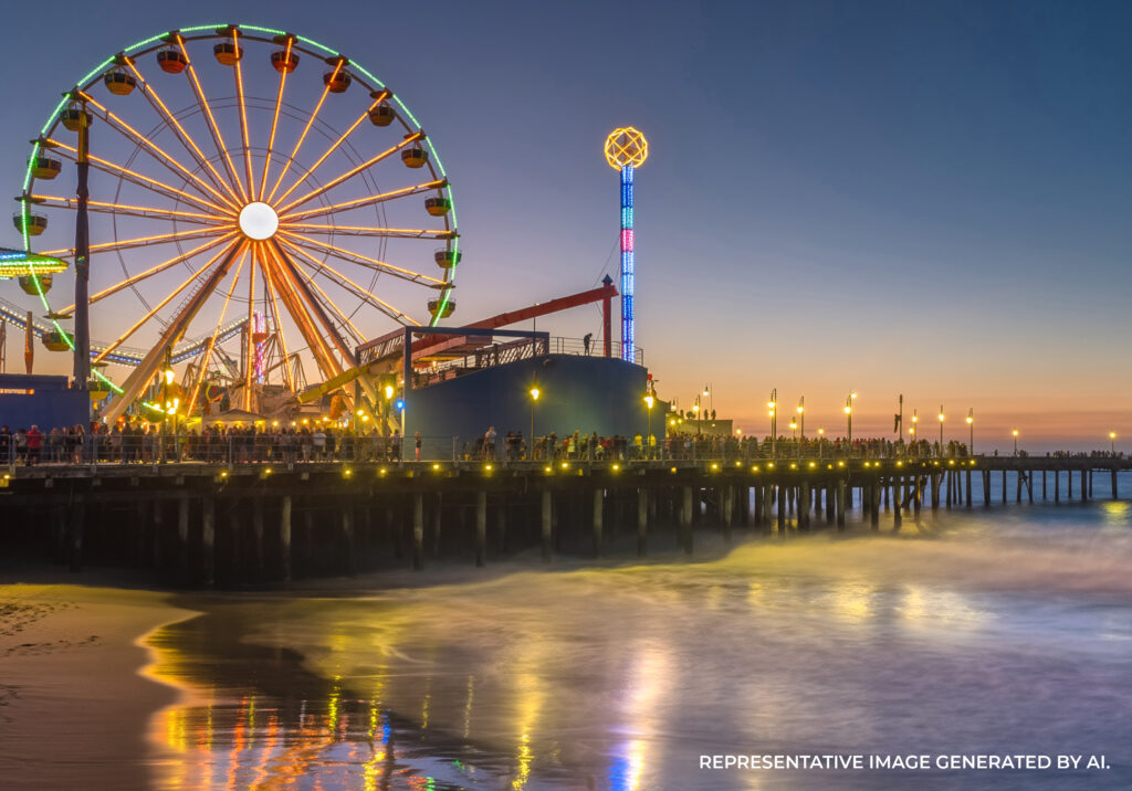 The Santa Monica Pier illuminated at night with reflections in the ocean and colorful lights on the ferris wheel.