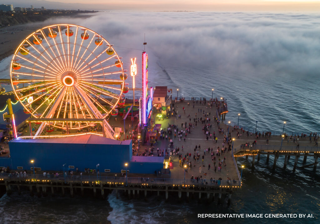 Aerial perspective of Santa Monica Pier with illuminated rides and ocean waves at twilight.