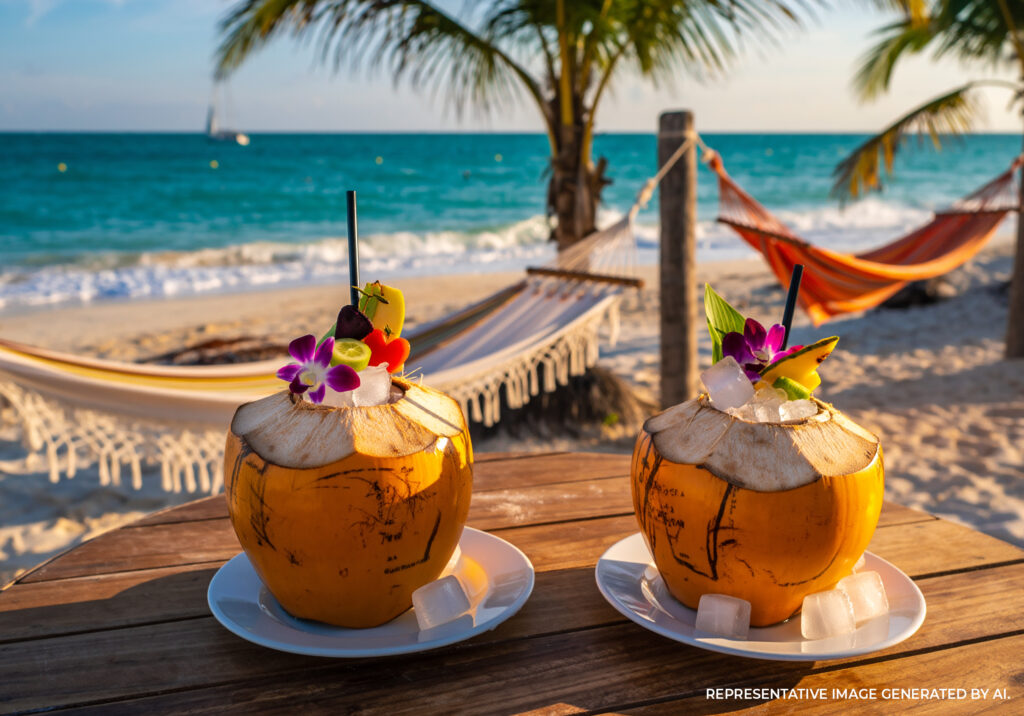 Two tropical cocktails served in coconuts on a beachside table overlooking the ocean in Tulum Mexico