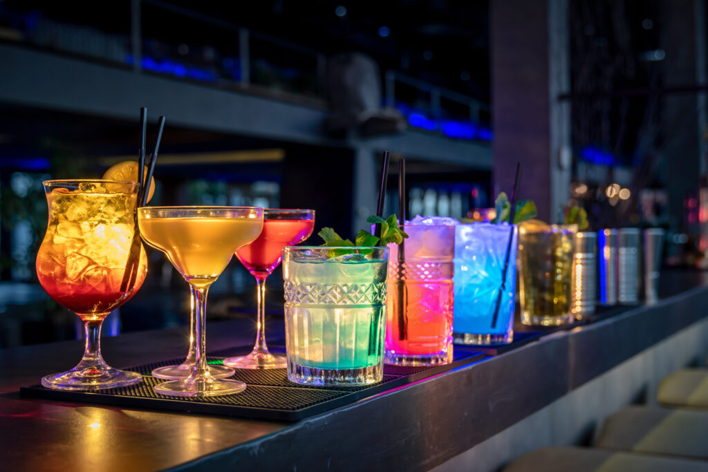 A row of bright cocktails illuminated by neon lighting on a modern bar counter.