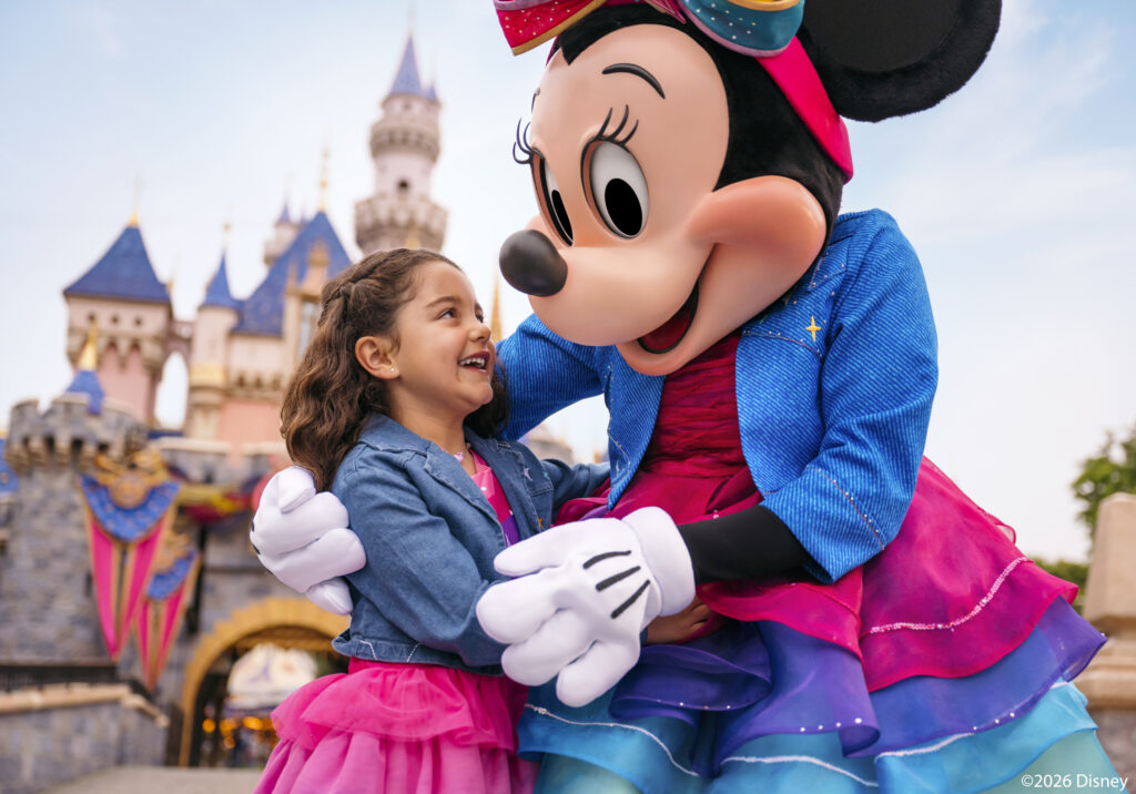 Minnie Mouse interacting with a child in front of Sleeping Beauty Castle at Disneyland® Park.