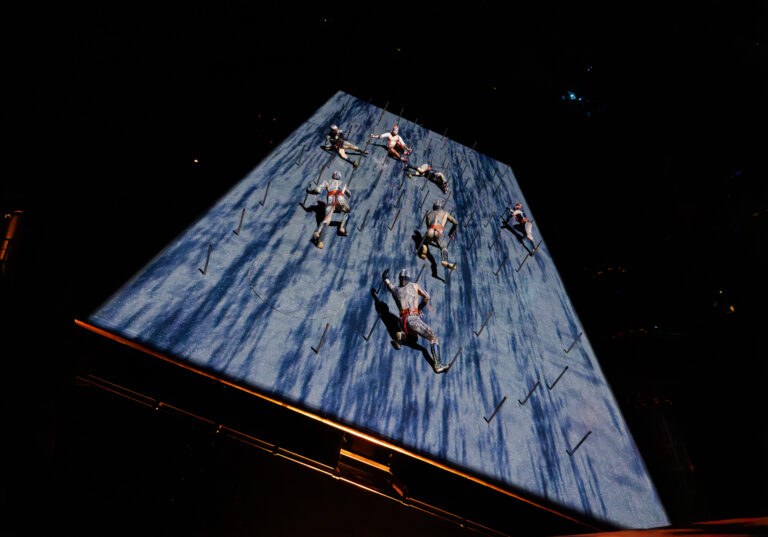 KA by Cirque du Soleil performers climbing a vertical stage wall during an intense acrobatic battle scene in Las Vegas
