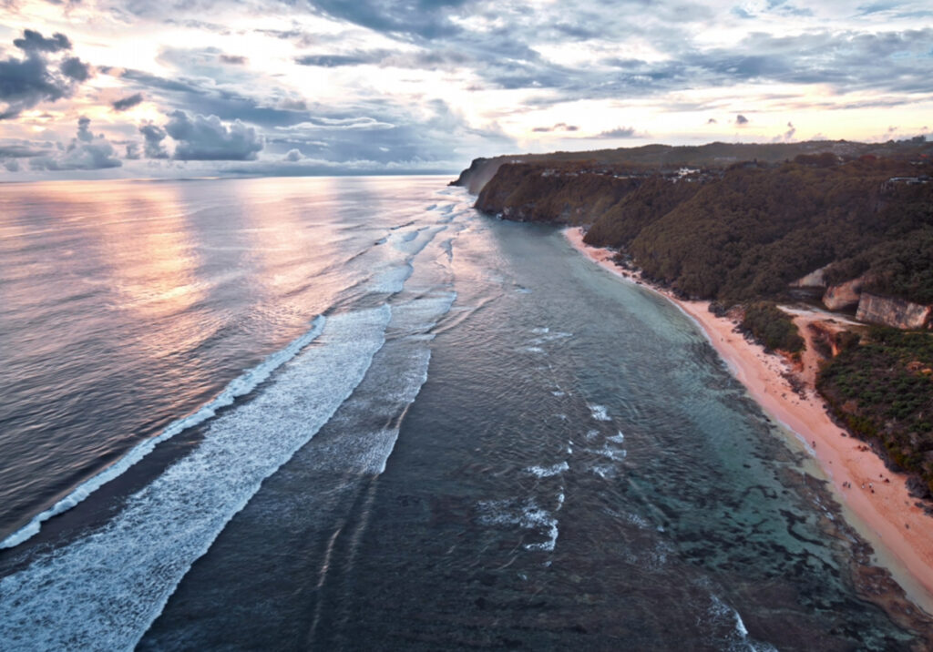 Aerial view of a secluded black sand beach with waves gently rolling toward shore under soft natural light.