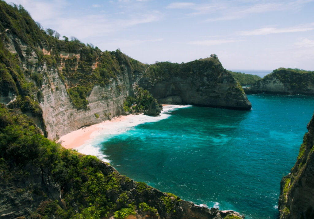 Hidden coastal cove with crystal clear turquoise water surrounded by lush green cliffs.