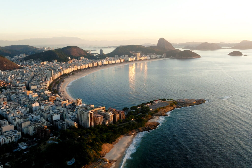 Aerial view of Copacabana Beach in Rio de Janeiro at golden hour with the city skyline and Sugarloaf Mountain in the distance