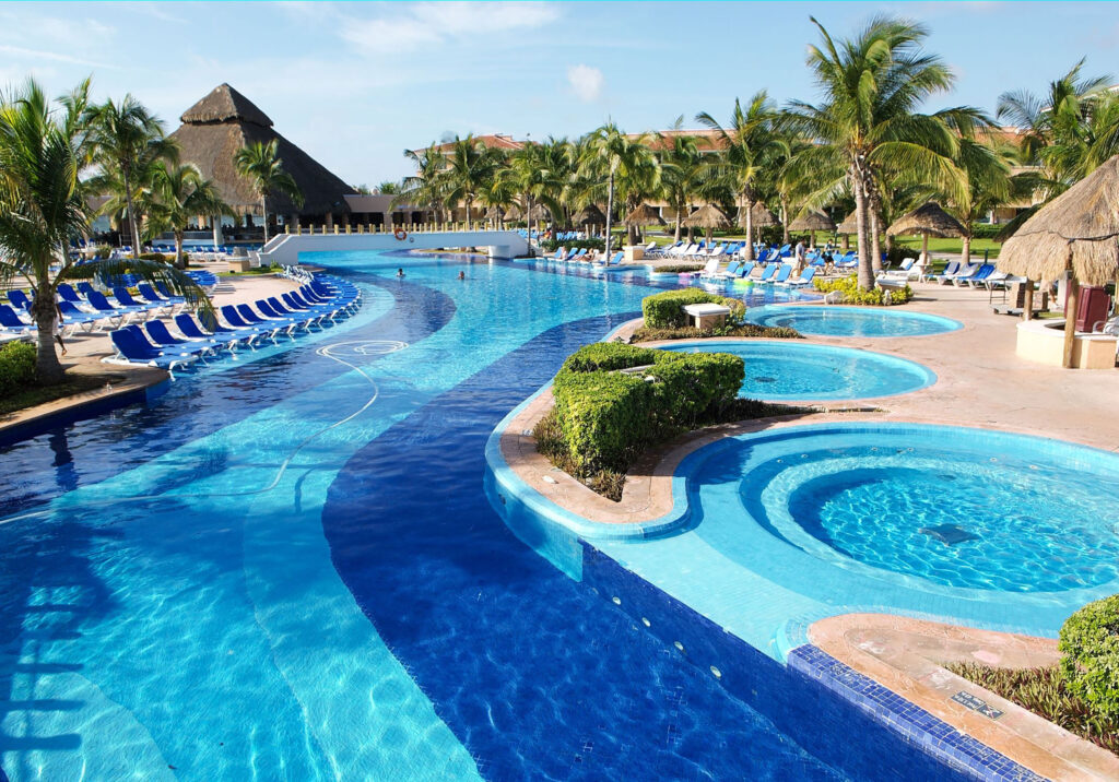 Large resort pool with curved design, lounge chairs, and tropical landscaping in Cancun