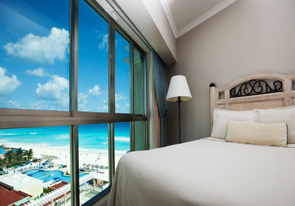 Hotel room with bed and large window overlooking ocean and resort pool