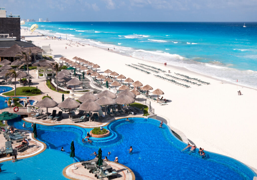 Resort pool and beachfront with lounge chairs and turquoise ocean in Cancun