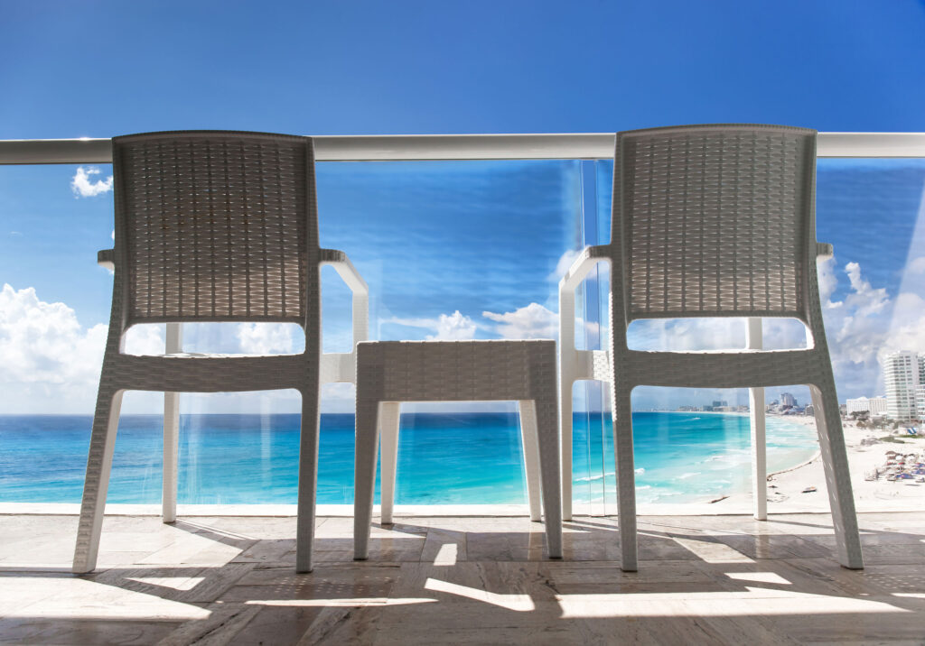 Two chairs on a private balcony overlooking turquoise ocean and white sand beach in Cancun