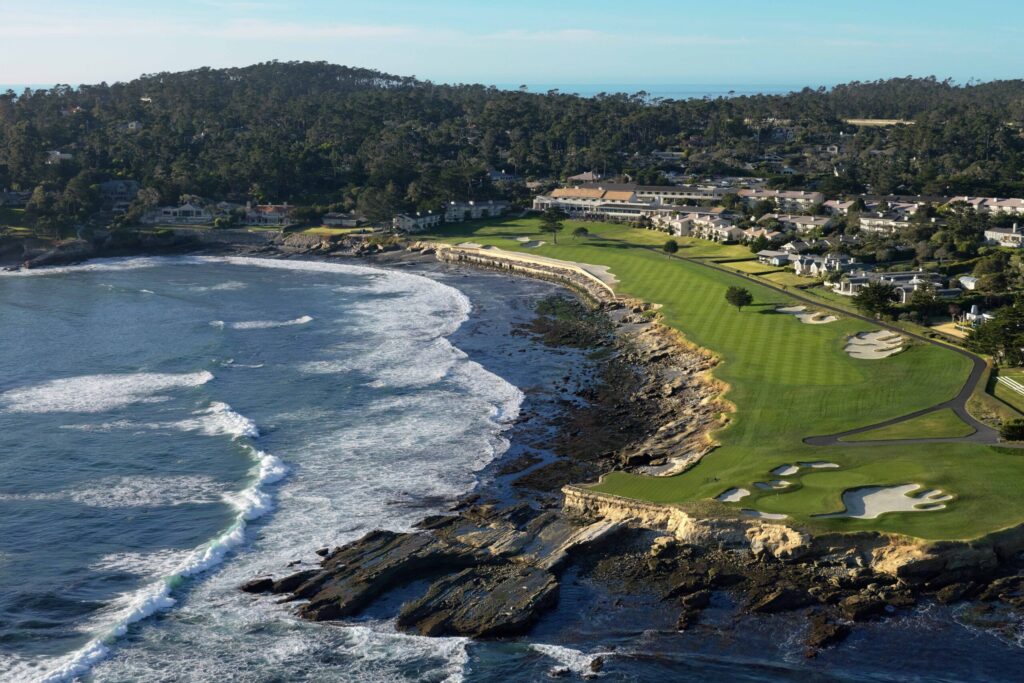 Aerial view of Pebble Beach Golf Links along the California coastline with fairways hugging the ocean.